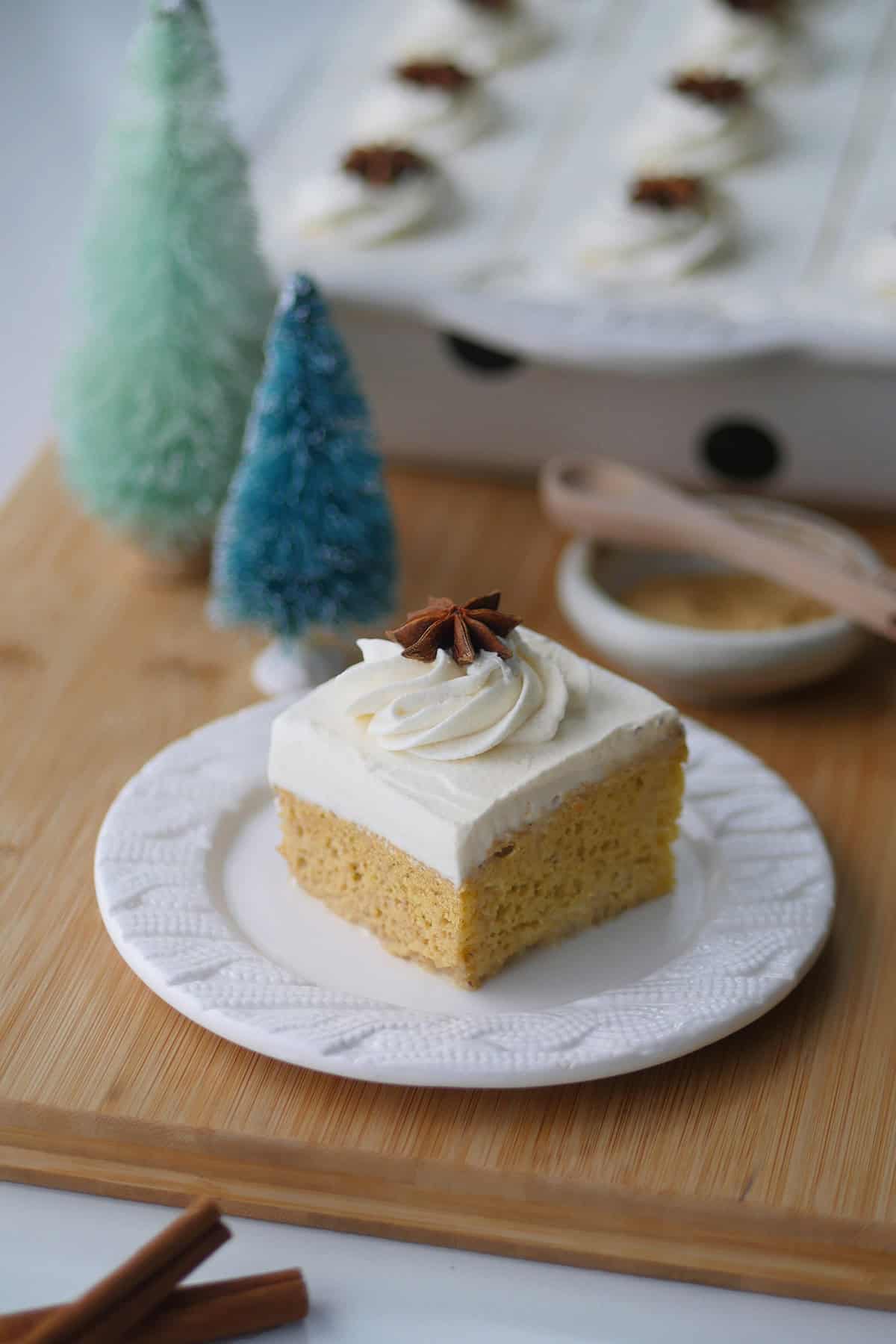 A slice of gingerbread 3 milk cake on a plate with an unfocused background of the whole sheet cake pan in the background.